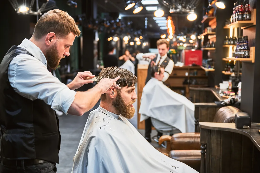 Inside a busy barbershop, a barber cutting a client's hair